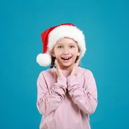 Image of Excited little child in Santa hat on light blue background. Christmas celebration