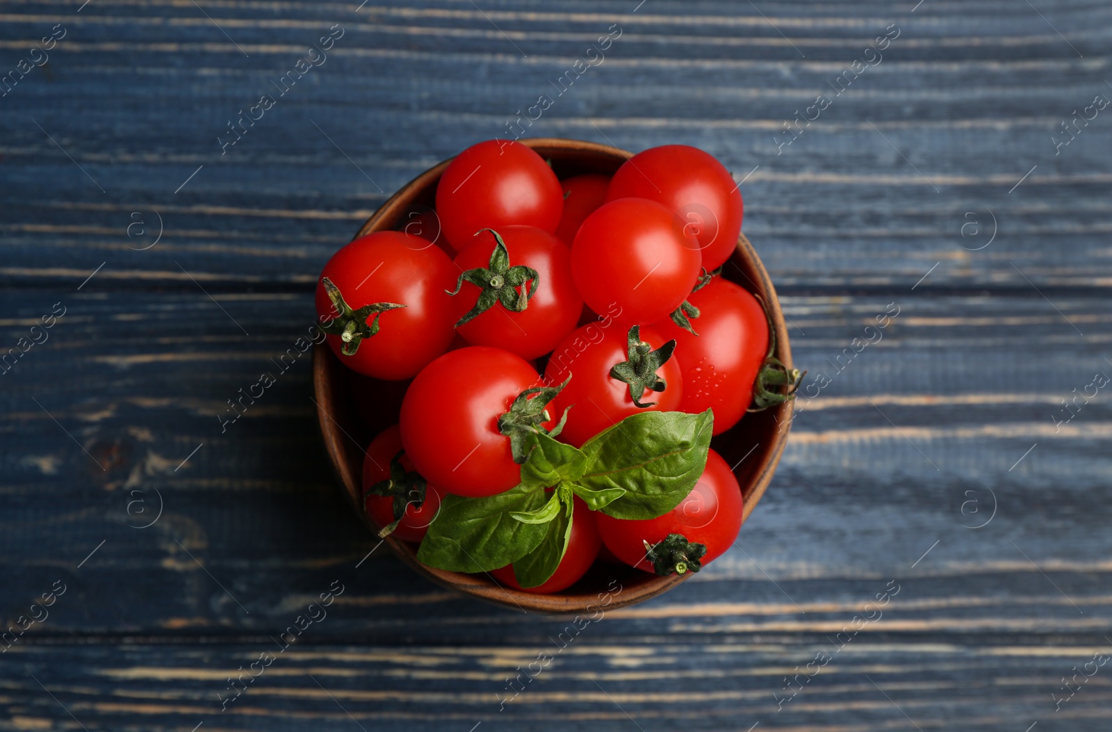 Photo of Fresh ripe cherry tomatoes and basil on blue wooden table, top view