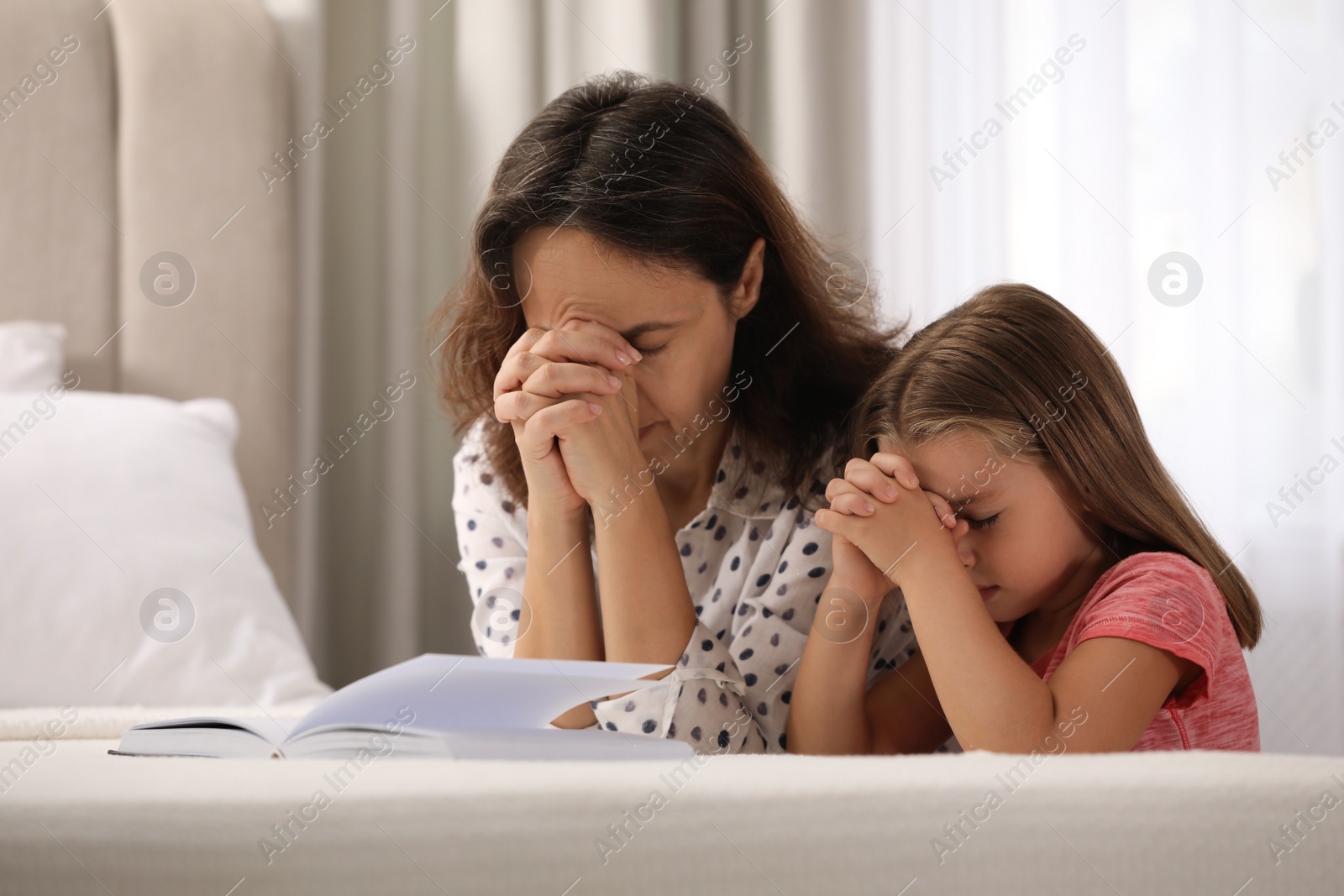 Photo of Mature woman with her little granddaughter praying together over Bible in bedroom