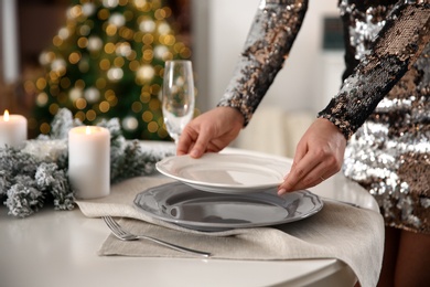 Young woman setting table for Christmas dinner at home, closeup