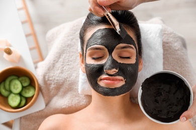 Photo of Cosmetologist applying black mask onto woman's face in spa salon, top view