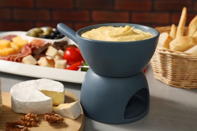 Fondue with tasty melted cheese and different snacks on grey table