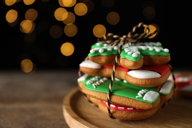 Photo of Tasty Christmas cookies on wooden table against black background with blurred lights, closeup