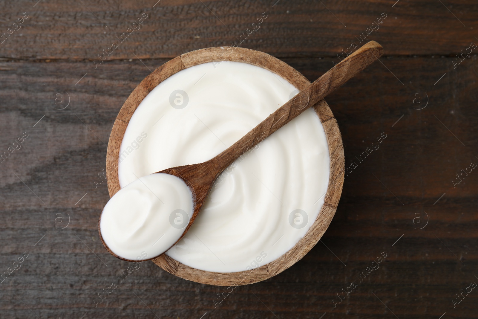 Photo of Delicious natural yogurt in bowl and spoon on wooden table, top view