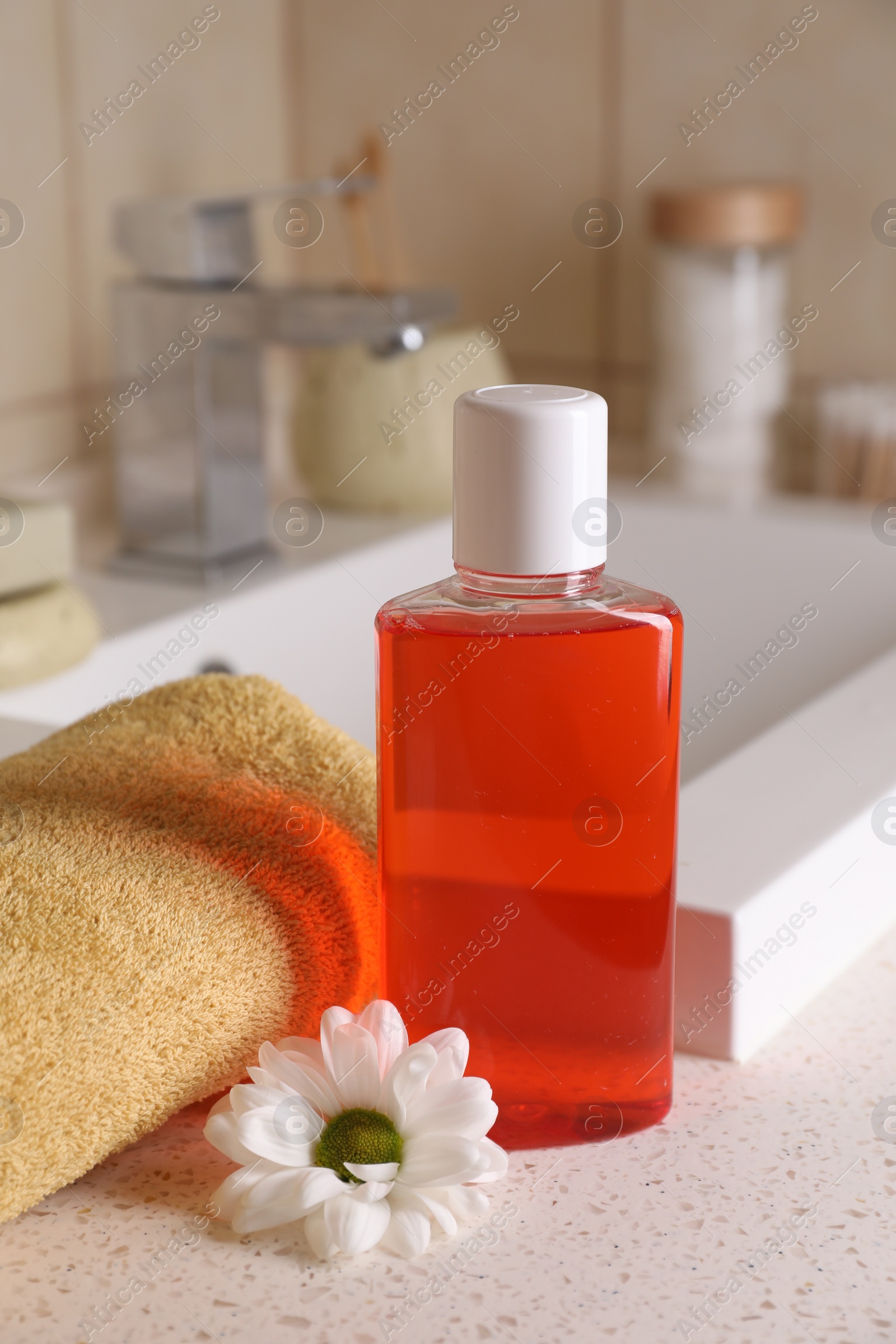 Photo of Fresh mouthwash in bottle, chamomile and towel on countertop near sink in bathroom, closeup