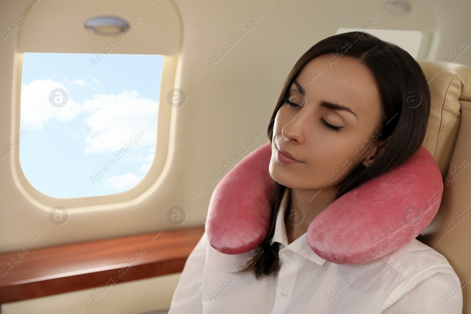 Photo of Young woman with travel pillow sleeping in airplane during flight