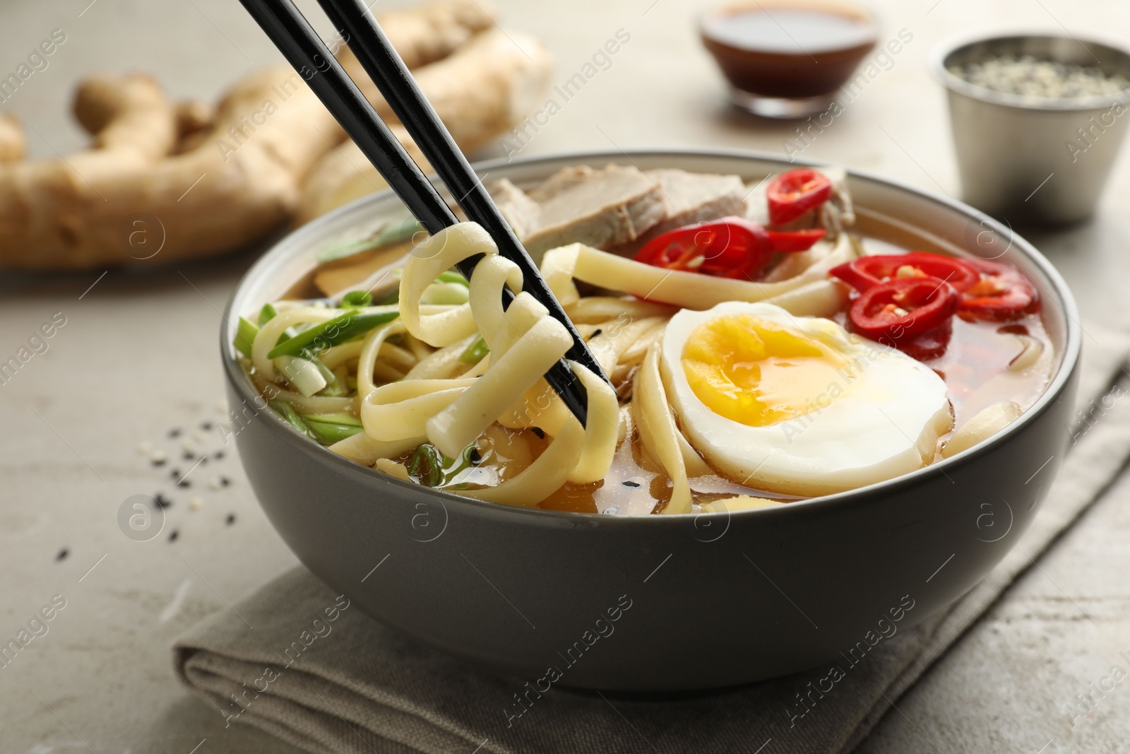 Photo of Eating delicious ramen with chopsticks at light table, closeup. Noodle soup