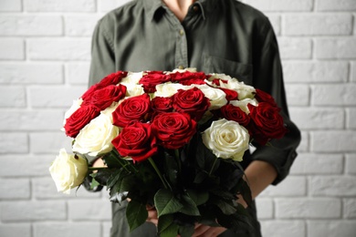 Woman holding luxury bouquet of fresh roses near white brick wall, closeup