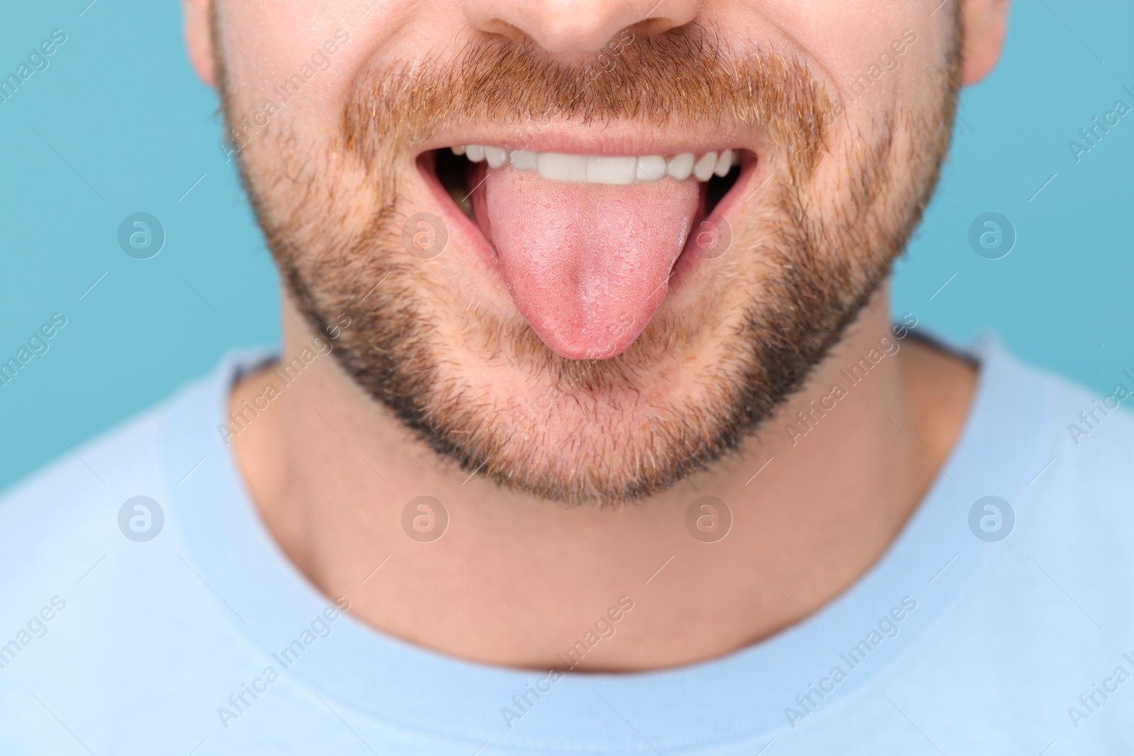 Photo of Man showing his tongue on light blue background, closeup