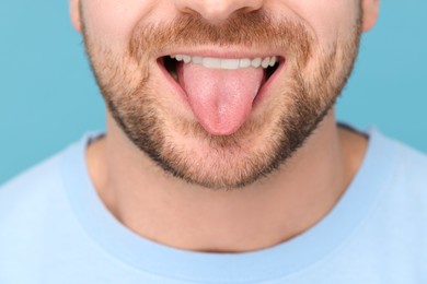 Photo of Man showing his tongue on light blue background, closeup