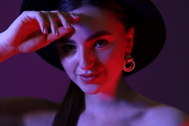 Photo of Portrait of beautiful young woman in hat on color background with neon lights, closeup