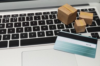 Photo of Internet shopping. Small cardboard boxes and credit card on laptop, closeup. Space for text