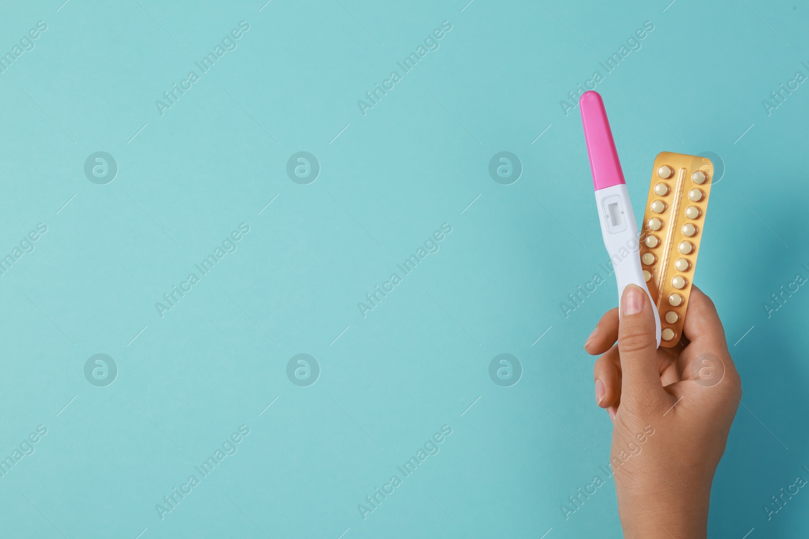 Photo of Woman holding birth control pills and pregnancy test on light blue, top view. Space for text