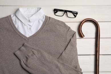 Elegant walking cane, sweater and glasses on white wooden table, flat lay