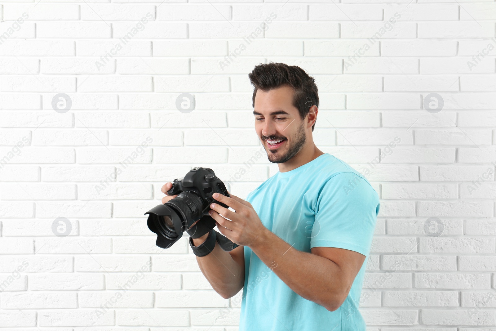 Photo of Young photographer with professional camera near brick wall