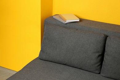 Photo of Books on grey sofa near yellow wall in room