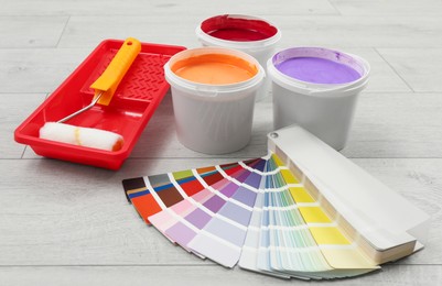 Photo of Buckets of paints, palette and decorator's tools on light wooden background