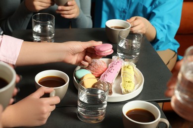 Photo of Friends with coffee and macarons spending time together in cafe, closeup