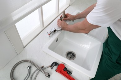 Professional plumber fixing water tap in kitchen, above view