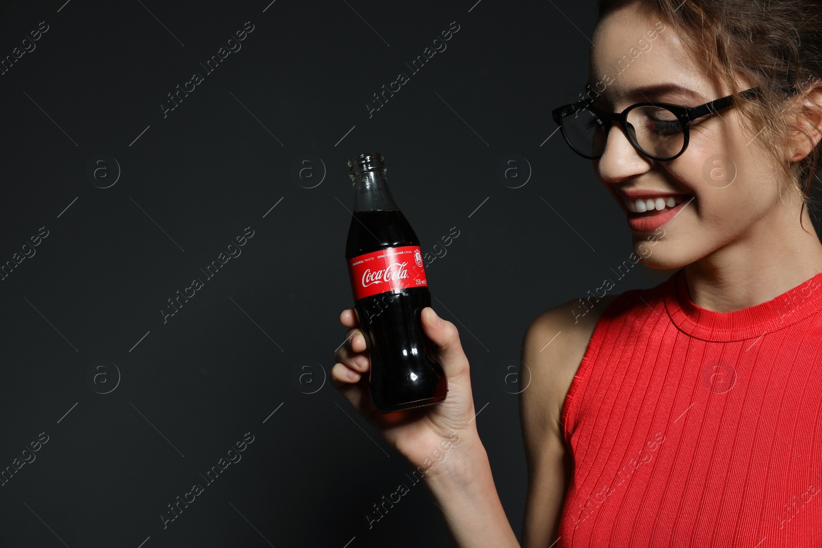 Photo of MYKOLAIV, UKRAINE - NOVEMBER 28, 2018: Young woman with bottle of Coca-Cola on dark background, space for text