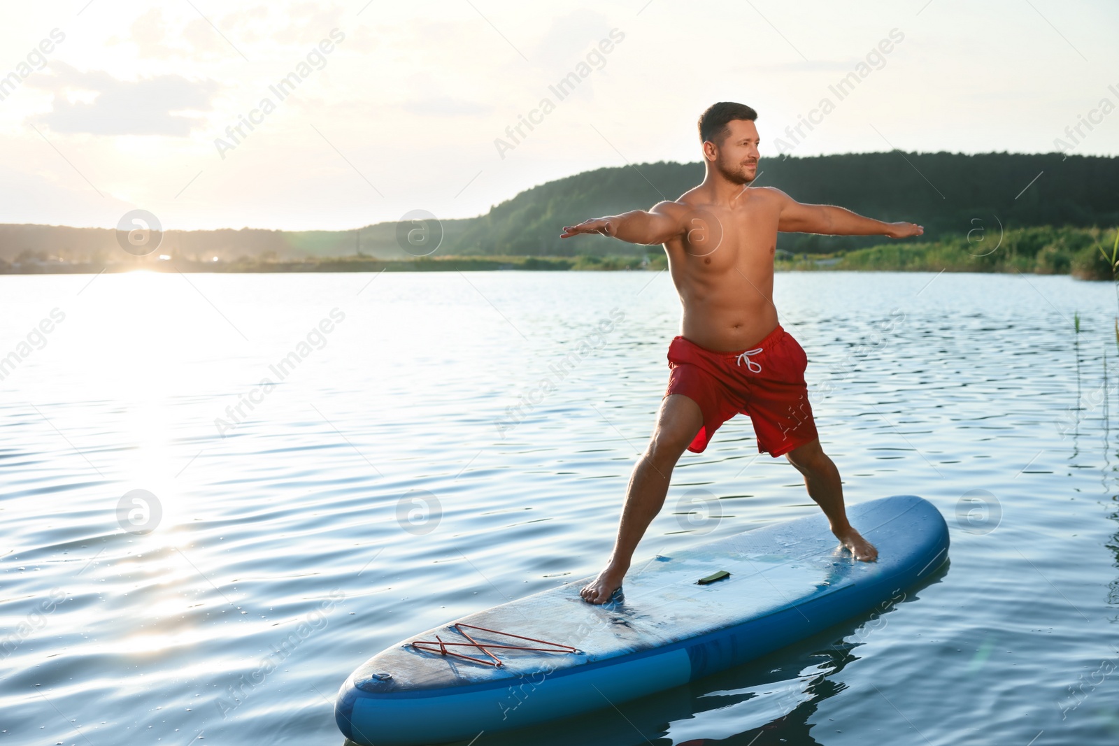 Photo of Man practicing yoga on light blue SUP board on river at sunset