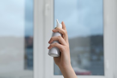 Photo of Woman holding nasal spray bottle indoors, closeup