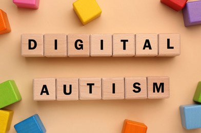 Photo of Phrase Digital Autism made of wooden cubes among colorful ones on beige background, flat lay. Addictive behavior