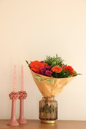 Photo of Bouquet of flowers and candles on wooden table near white wall