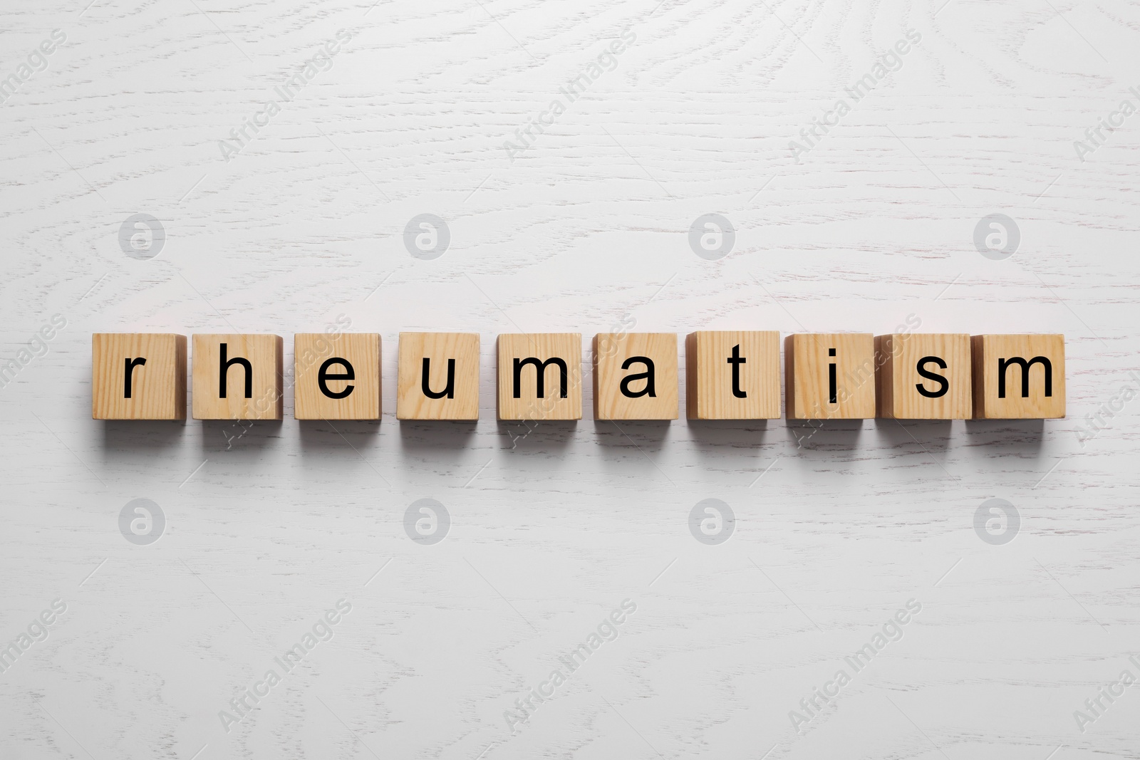 Photo of Word Rheumatism made of cubes on white wooden table, top view