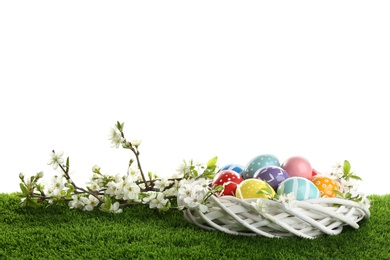 Photo of Painted Easter eggs in nest and blossoming branches on green grass against white background