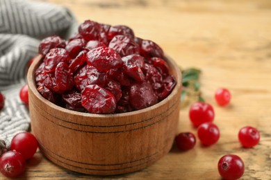 Photo of Tasty dried cranberries in bowl and fresh ones on wooden table, closeup