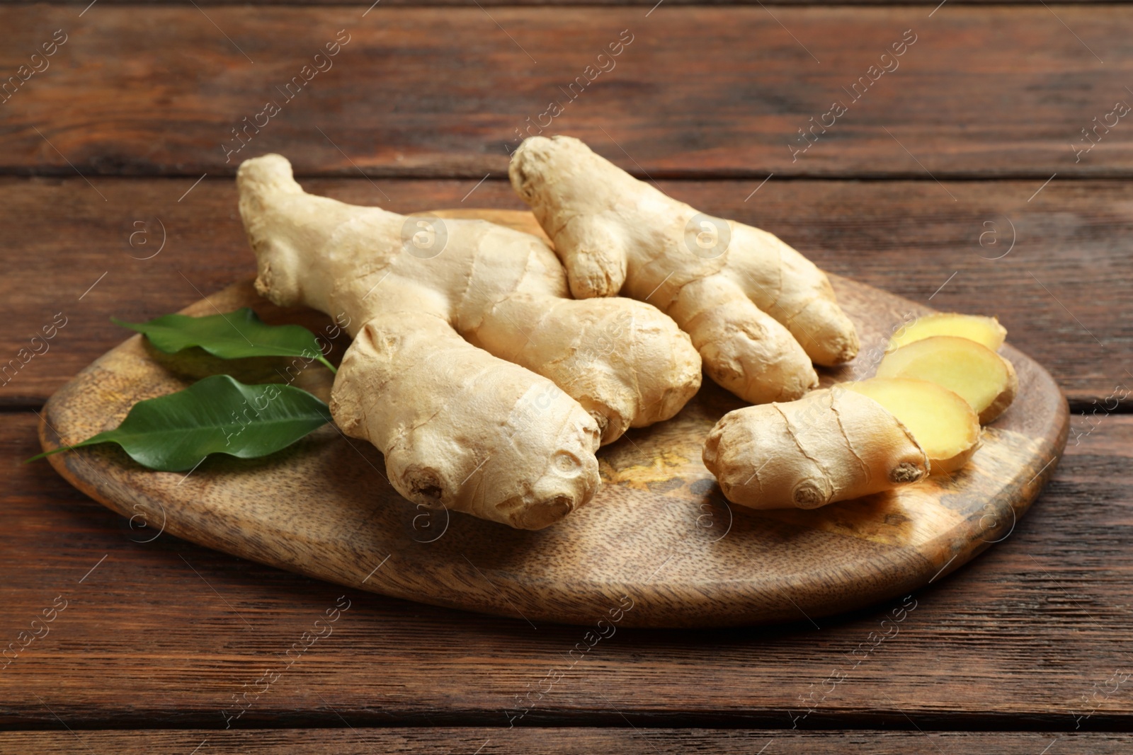 Photo of Cut and whole fresh ginger with leaves on wooden table