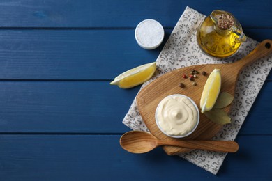 Tasty mayonnaise in bowl, products and spoon on blue wooden table, flat lay. Space for text