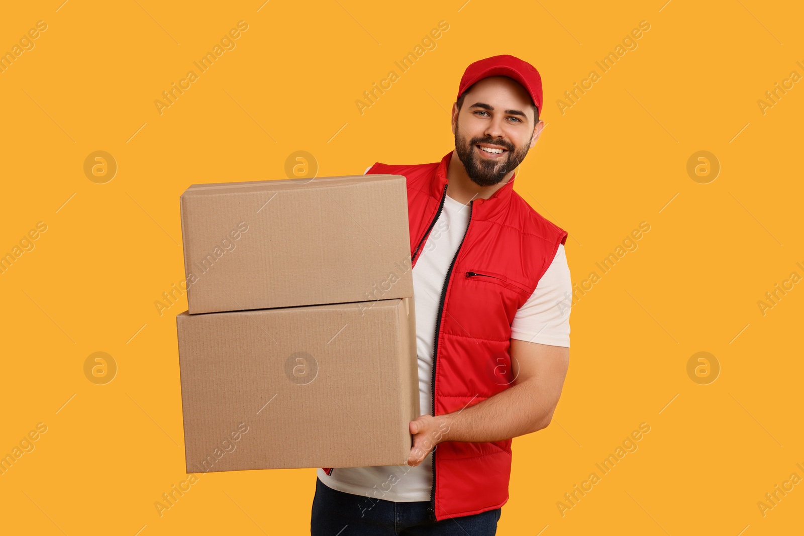 Photo of Happy young courier with parcels on orange background