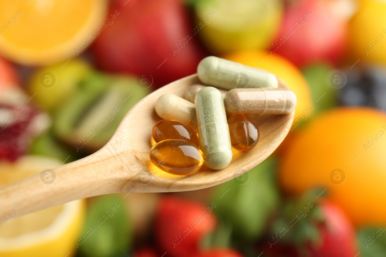 Photo of Different vitamin pills in spoon over fresh fruits, closeup