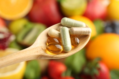 Different vitamin pills in spoon over fresh fruits, closeup