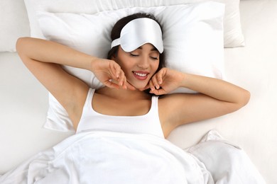 Photo of Beautiful young woman with sleeping mask lying in bed, top view