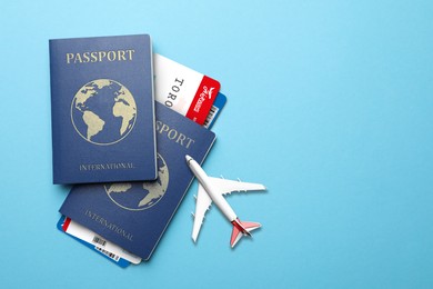 International passports, boarding passes and airplane model on light blue background, flat lay. Space for text