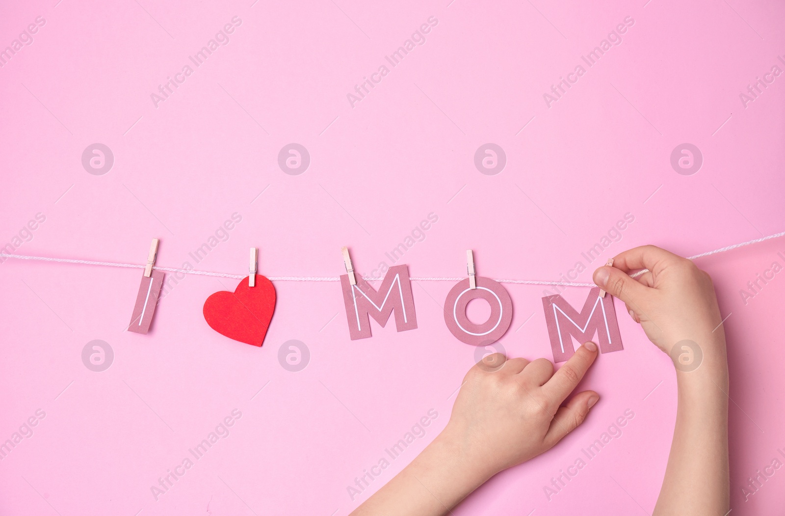 Photo of Child hanging phrase "I LOVE MOM" made of paper letters on rope against color background. Happy Mother's Day