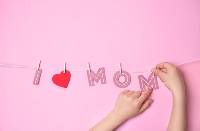 Photo of Child hanging phrase "I LOVE MOM" made of paper letters on rope against color background. Happy Mother's Day