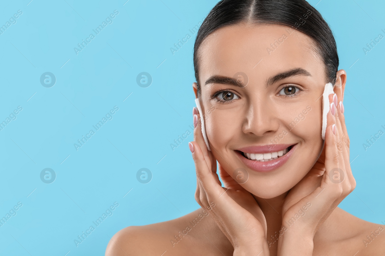 Photo of Beautiful woman removing makeup with cotton pads on light blue background. Space for text