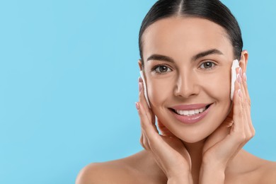 Photo of Beautiful woman removing makeup with cotton pads on light blue background. Space for text