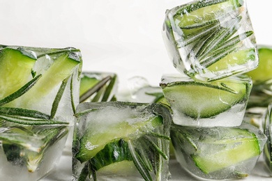 Ice cubes with cut cucumber and rosemary on light background, closeup