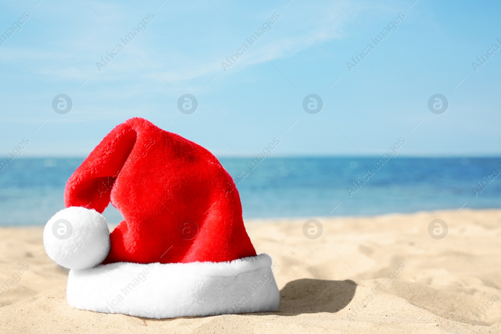 Photo of Santa's hat on sandy beach, space for text. Christmas vacation