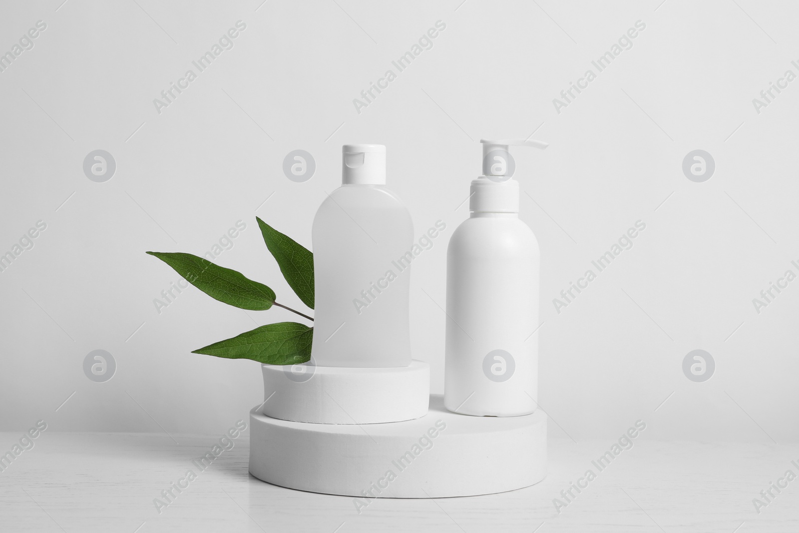 Photo of Bottles of cosmetic products and leaves on white wooden table