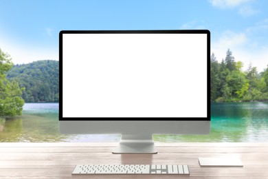 Image of Modern computer with blank screen on wooden table and view of beautiful river and mountains