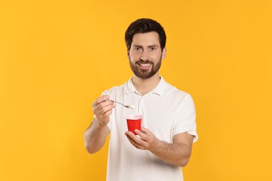 Photo of Handsome man with delicious yogurt and spoon on yellow background