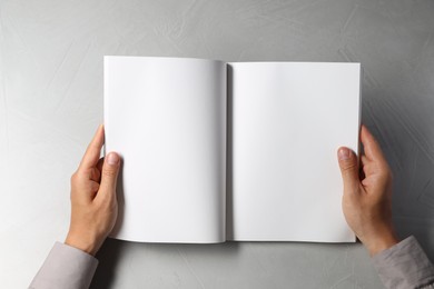 Photo of Man holding blank book at light grey table, top view. Mockup for design