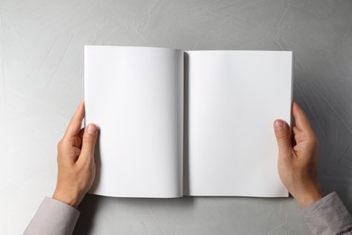 Man holding blank book at light grey table, top view. Mockup for design