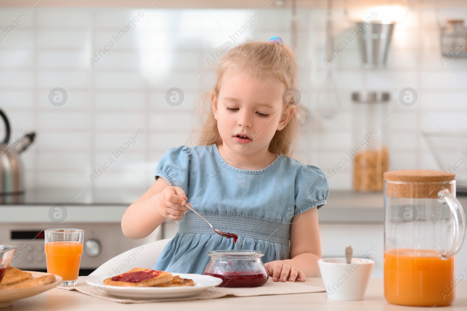 Photo of Cute little girl with tasty toasted bread and jam at table in kitchen